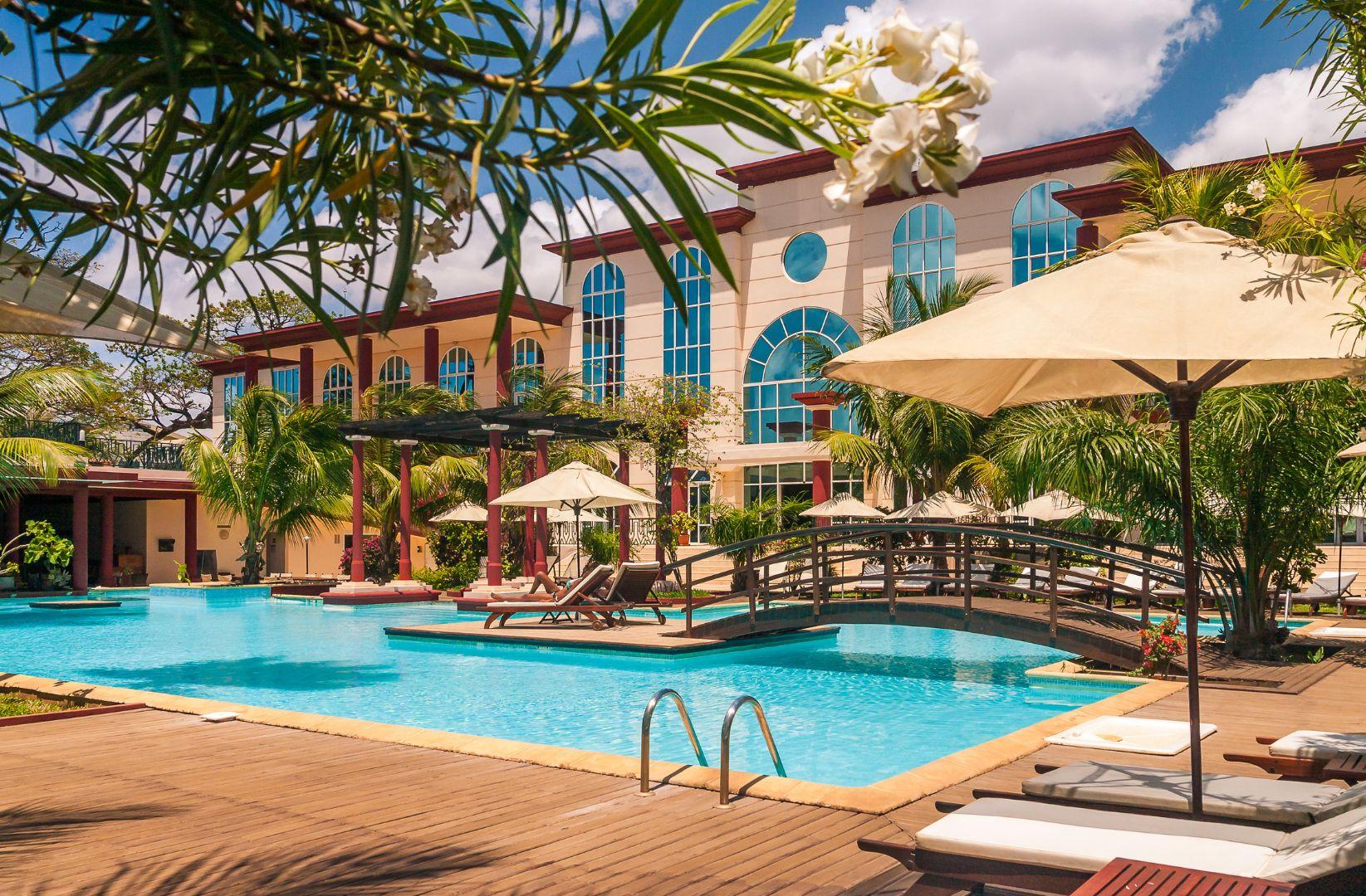 Piscina rodeada de palmeras frente al edificio del hotel